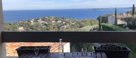 A balcony with a table set for two, overlooking a coastal town and the sea.