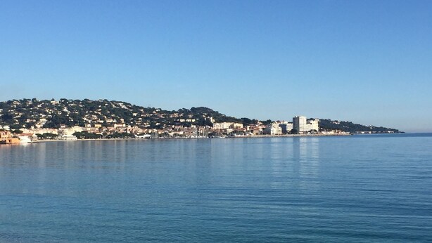 A coastal town with a clear view of the sea, a sandy beach, and buildings on a hillside.