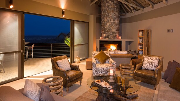 A spacious living area with a fireplace, comfortable seating, and a large glass door leading to a balcony with a view of the ocean. - Safarihoek (Kamanjab)