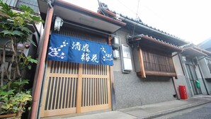 A traditional Japanese building with a wooden sliding door and a blue awning with white text. - (Guest House) Kiyomori no Baika (Shimogyo Ward)