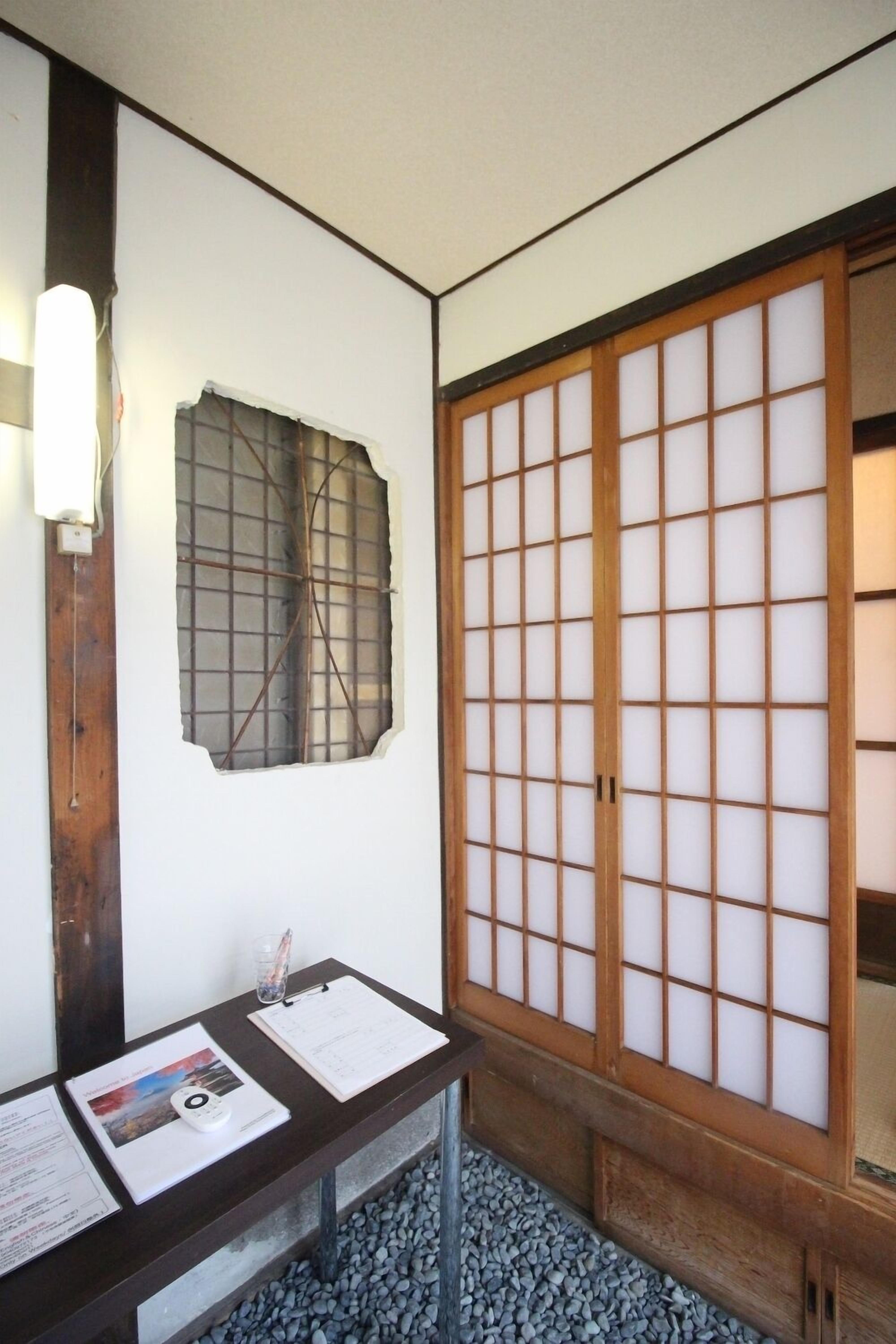 A traditional Japanese room with tatami flooring, a shoji screen, and a wooden desk with papers and a book.