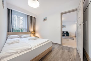 A modern bedroom with a large bed, a bedside table with a lamp, a window with curtains, and a view of another room. - Sun & Snow Rezydencja Ustronie Morskie (Ustronie Morskie)