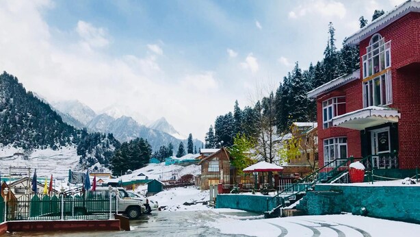 Un pueblo cubierto de nieve con edificios tradicionales, una carretera pavimentada y montañas al fondo.