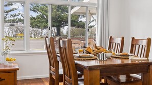 A dining area with a wooden table set for breakfast, including bread, fruits, and a coffee cup. - Pippi House - A Quintessential Beach House Opposite Pippi Beach - Holiday Yamba (YAMBA)