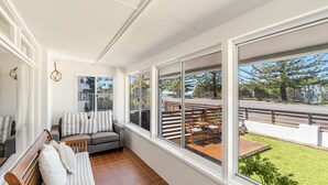 A sunlit room with a large window overlooking a deck and garden. - Pippi House - A Quintessential Beach House Opposite Pippi Beach - Holiday Yamba (YAMBA)