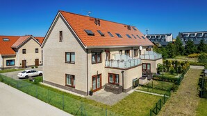 A two-story house with a red-tiled roof, a balcony, and a fenced yard with a car parked outside. - Apartamenty Sun & Snow Osiedle Wybrzeże (Ustronie Morskie)