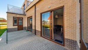 A modern brick house with a balcony, large sliding glass doors, and a visible outdoor area. - Apartamenty Sun & Snow Osiedle Wybrzeże (Ustronie Morskie)