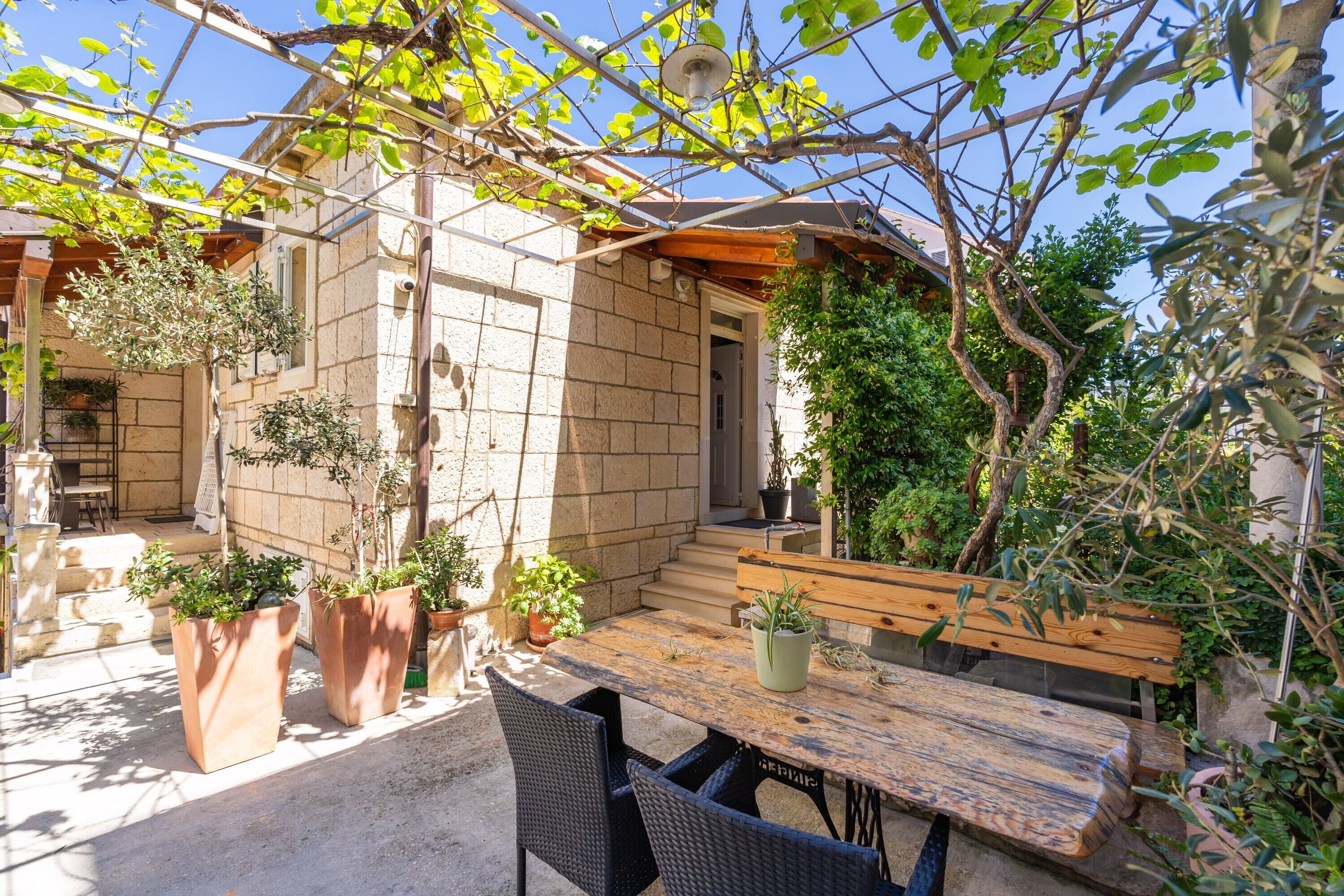 A patio with a wooden table and chairs, surrounded by potted plants and a stone wall.