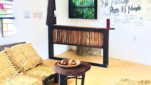 Una habitación con un sofá tejido, un taburete de madera con un plato de comida, un banco de madera oscura y una pared con una planta verde y texto escrito a mano.