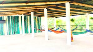 Un espacio al aire libre techado con columnas de bambú y hamacas.