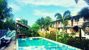 Una piscina con borde a cuadros, rodeada de exuberante vegetación y un edificio con balcones.