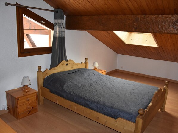 Ein hölzernes Bett in einem Raum mit schrägverlaufender Decke und einem Oberlicht.