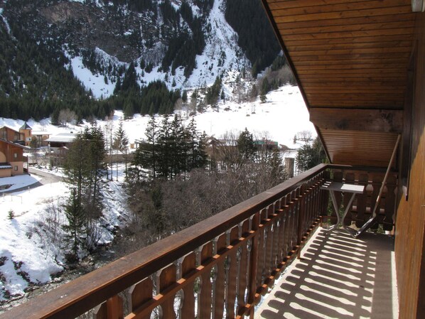A wooden balcony with a view of a snowy mountain and a village below.