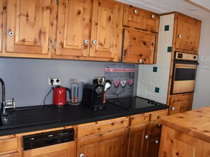 Eine Küche mit Holzausstattung, einem Geschirrspüler von Bosch, einer roten Kaffeemaschine, einem schwarzen Toaster und einem alten Ofen.