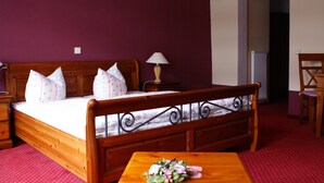 A wooden bed with a headboard, a bedside table with a lamp, and a floral arrangement on a wooden table. - Pension & Restaurant Zum Echten (Bautzen)
