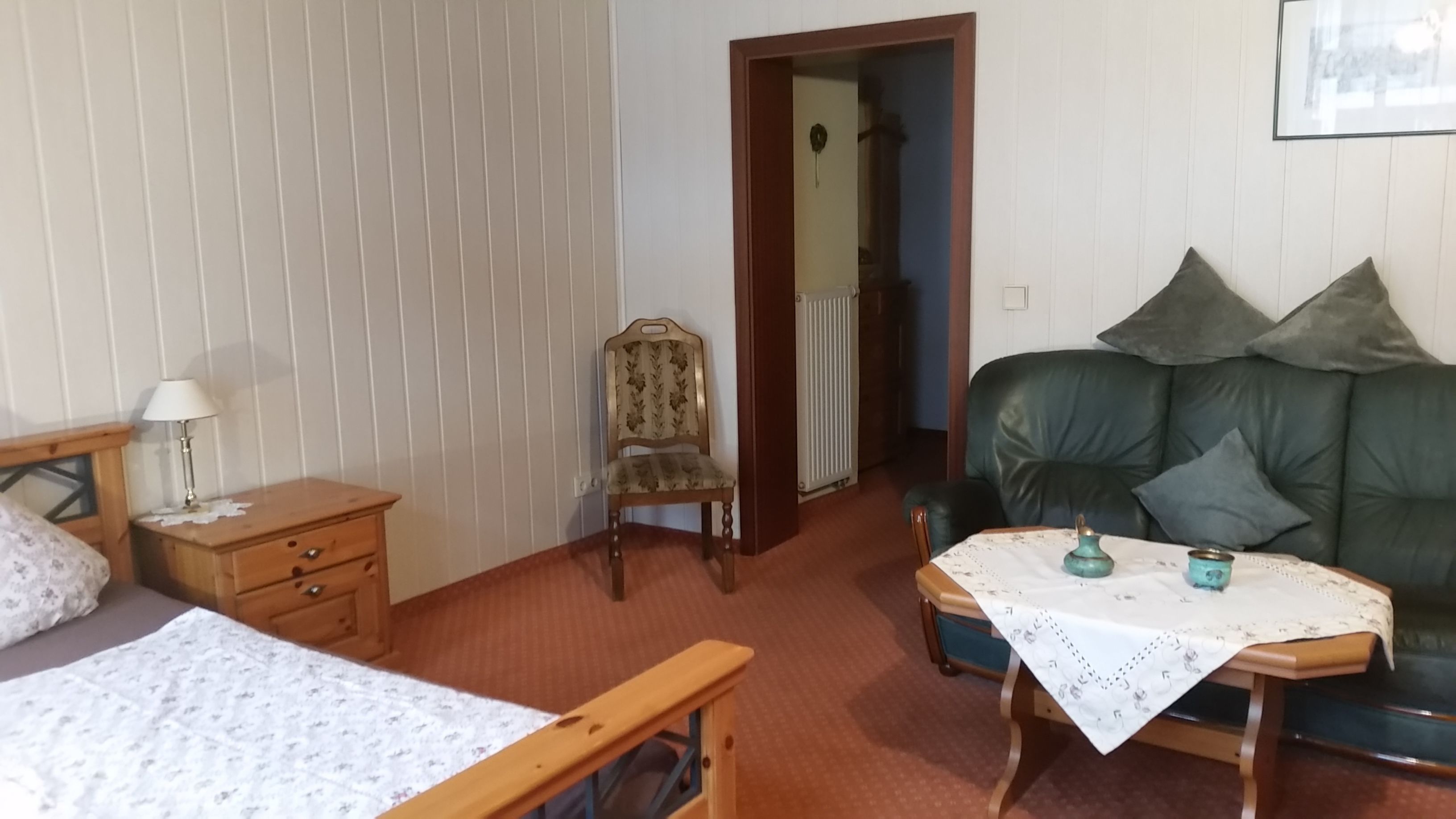 A cozy room with a bed, a wooden nightstand, a chair, a green sofa, and a small table with a tablecloth.