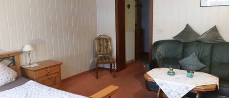 A cozy room with a bed, a wooden nightstand, a chair, a green sofa, and a small table with a tablecloth.