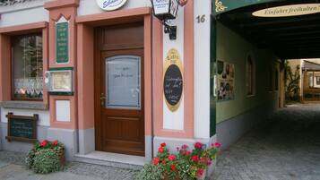 A traditional European building with a wooden door, signs for 'Eibauer' and 'Pension', and flower boxes on the ground.