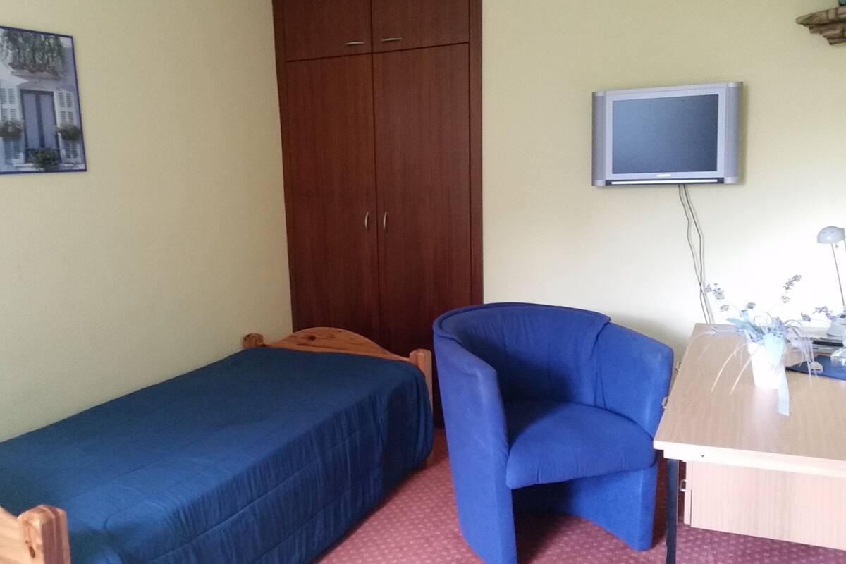 A small room with a single bed, a desk with a computer, a chair, and a wardrobe.