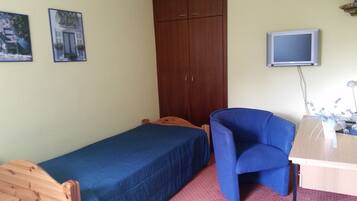 Ein kleines Zimmer mit einem Einzelbett, einem Schreibtisch mit Computer, einem Stuhl und einem Kleiderschrank.