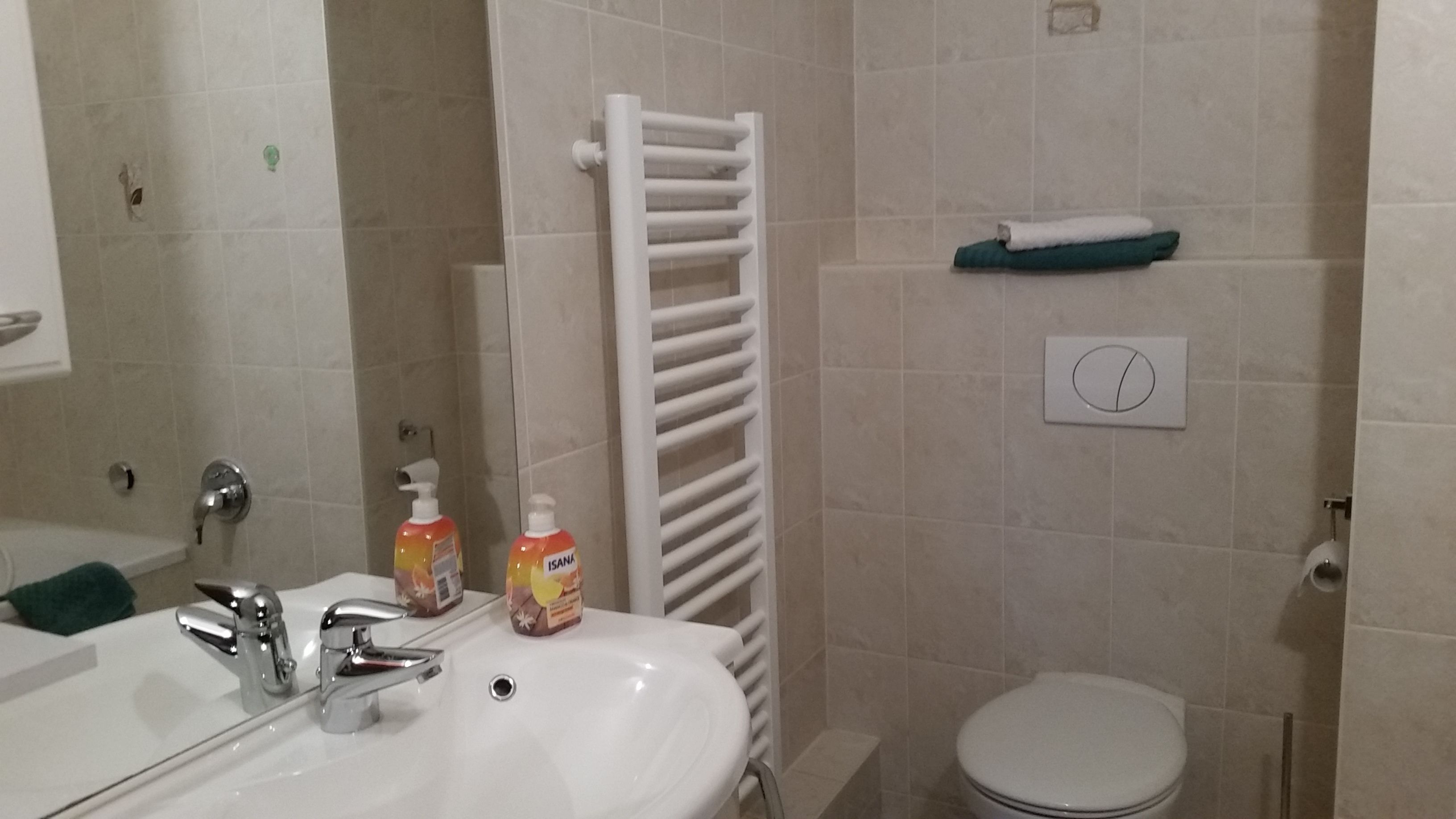 A bathroom with a white sink, a mirror, a towel rack, a toilet, and a shelf with a towel.