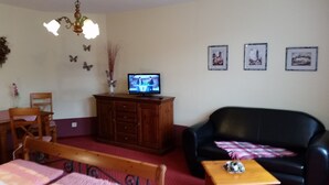 A living room with a wooden cabinet, a television, a black leather sofa, and a wooden table. - Pension & Restaurant Zum Echten (Bautzen)