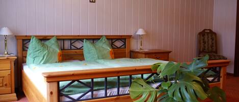 Una cama de madera con ropa de cama verde, dos lámparas de noche y una planta en maceta.