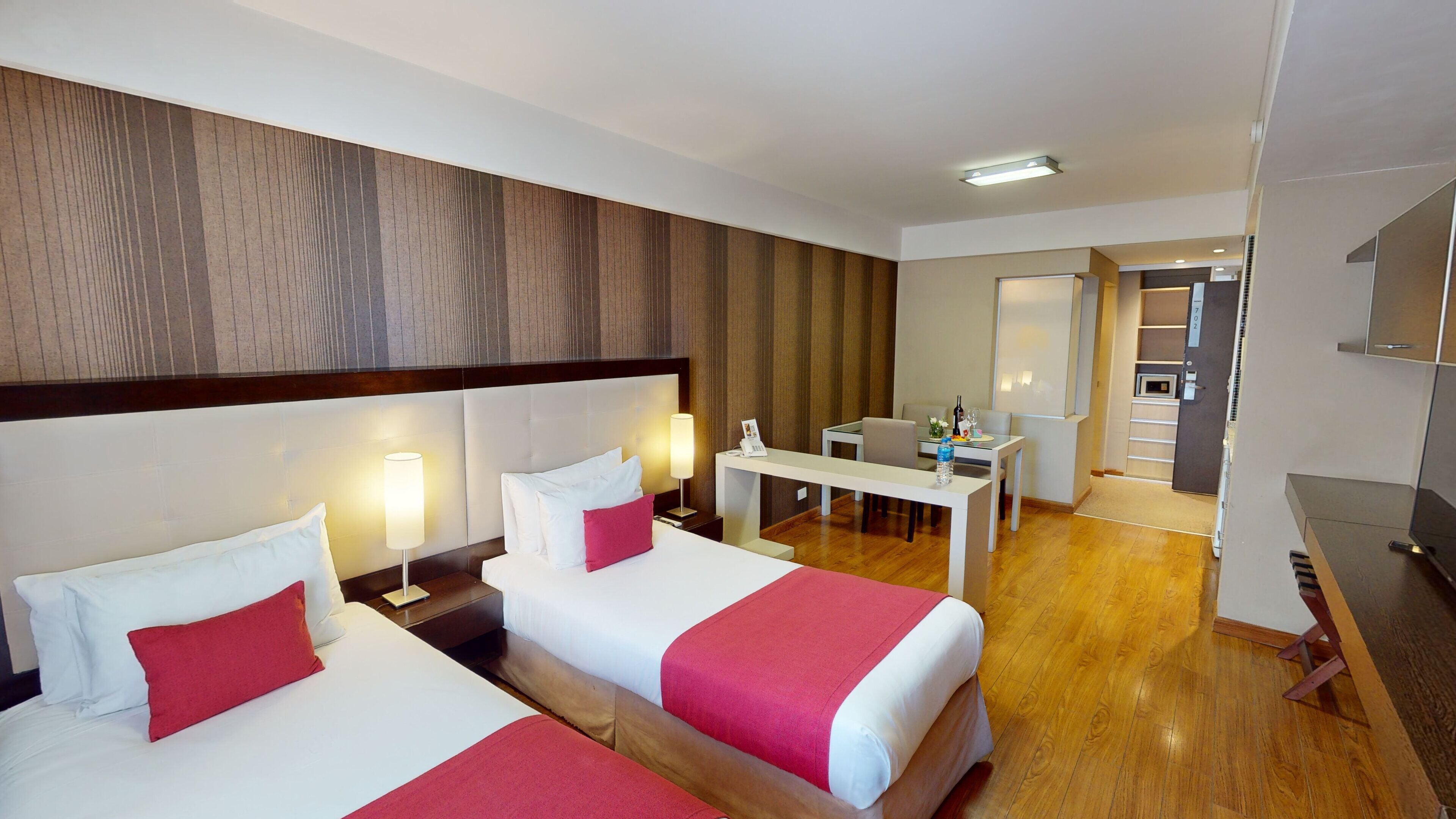 A hotel room with two beds, a desk, and a kitchenette.