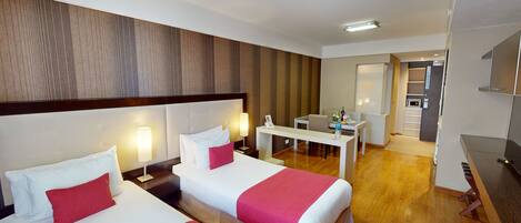 A hotel room with two beds, a desk, and a kitchenette.