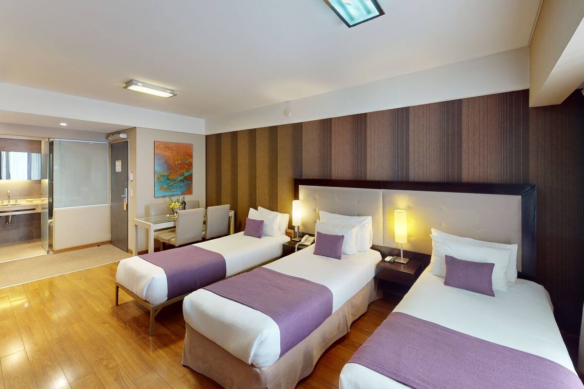 A hotel room with three beds, a desk, and a shower area.