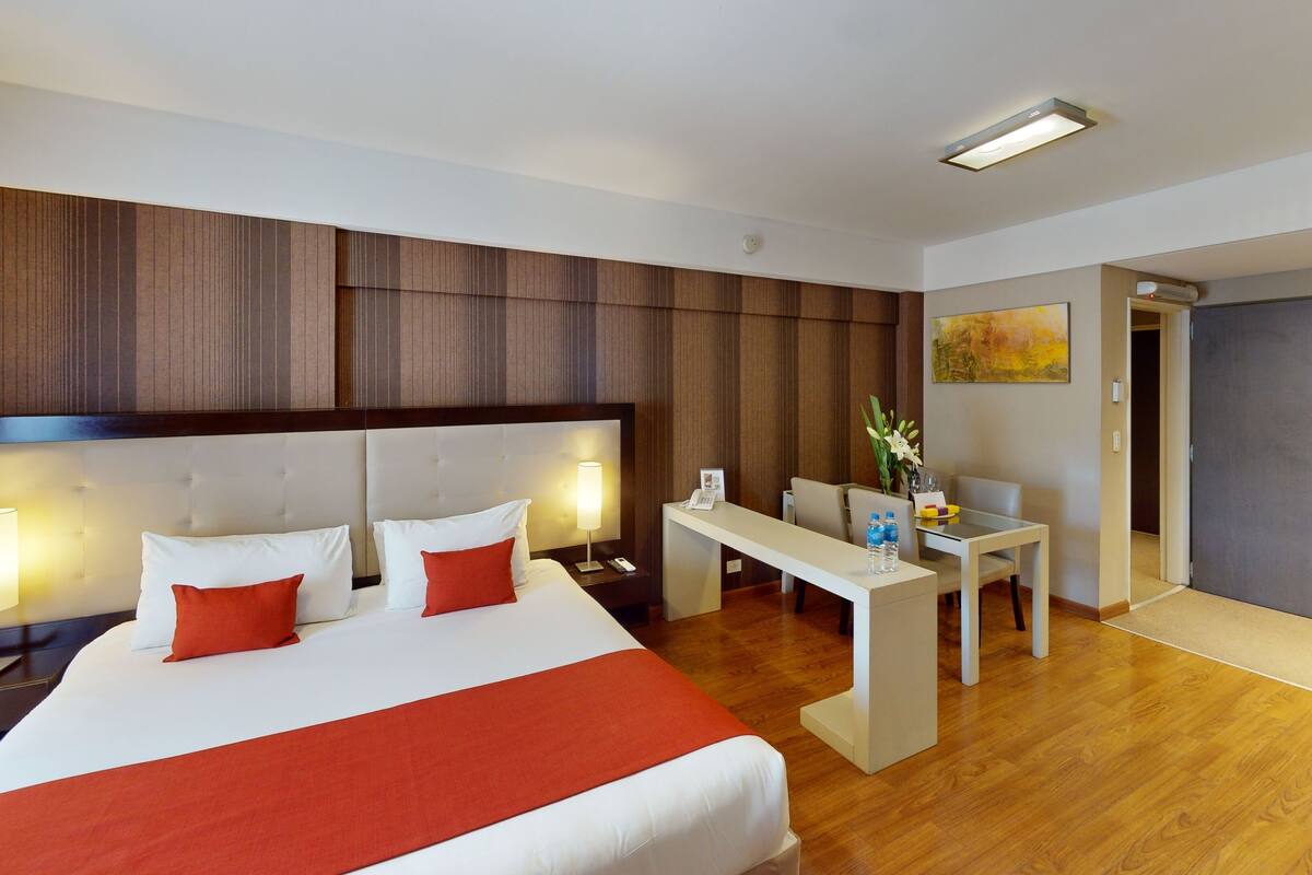 A hotel room with a large bed, bedside tables, a desk, and a chair.
