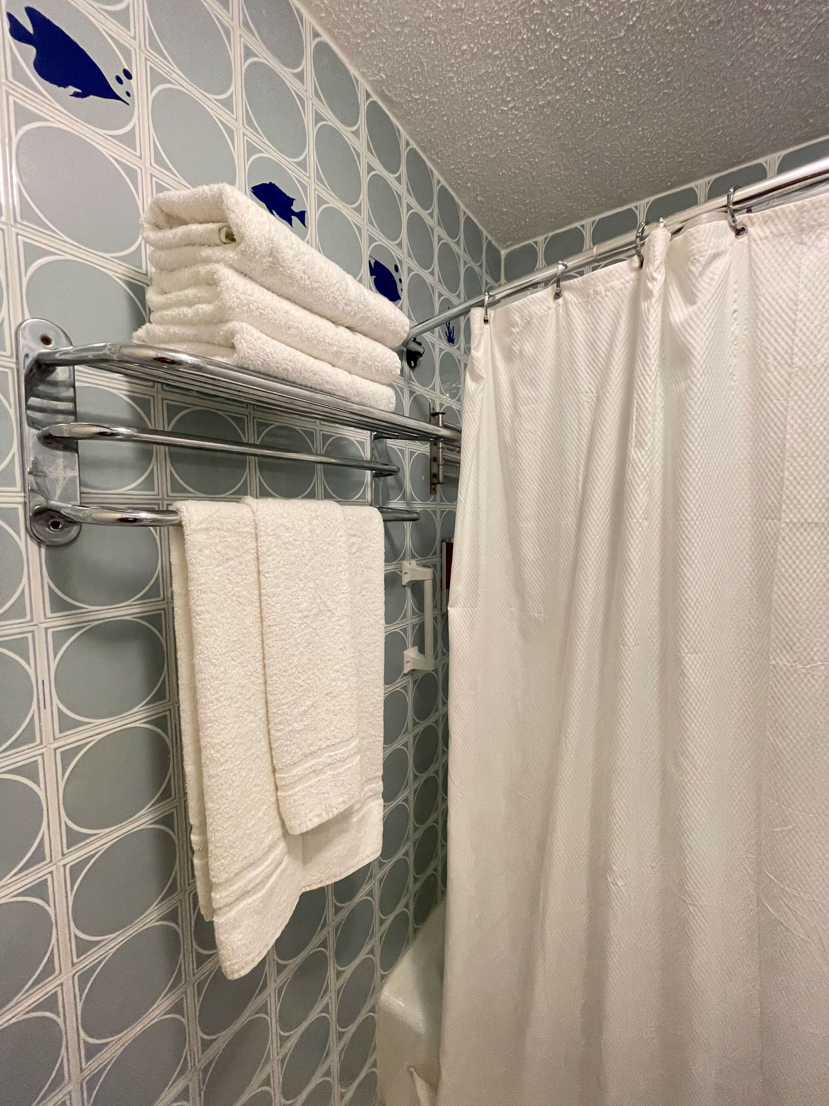 Un baño con pared decorada, un toallero de metal con toallas dobladas y una cortina de ducha.