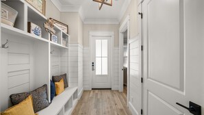 Un pasillo con una puerta blanca, estanterías decoradas y un banco con cojines.