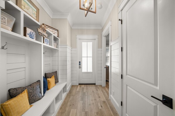Un pasillo con una puerta blanca, estanterías decoradas y un banco con cojines.