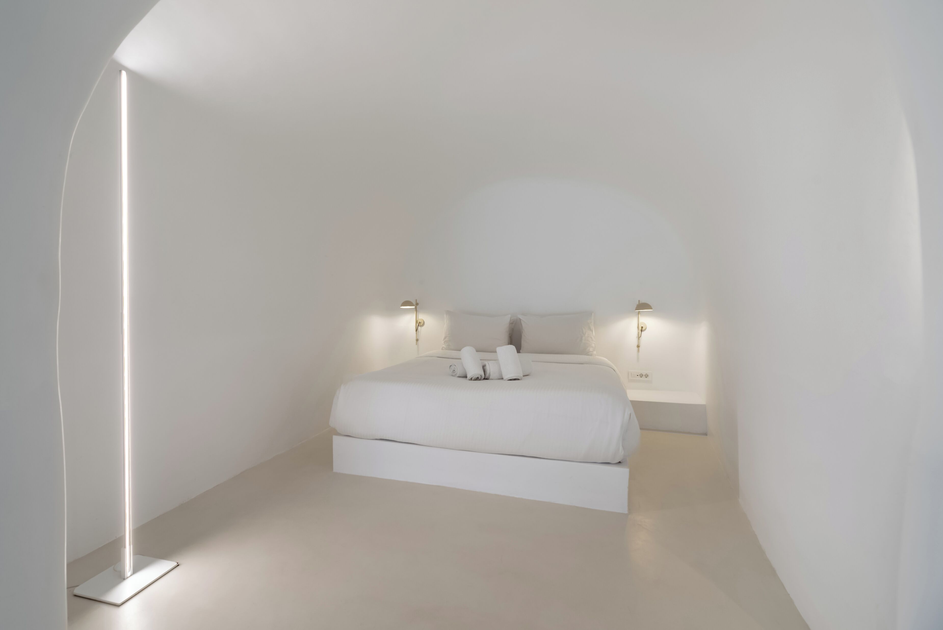 Un dormitorio minimalista con cama, lámparas de noche y una lámpara de pie.