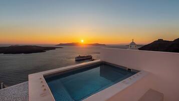 Una piscina con vistas a la puesta de sol sobre el mar y un pequeño edificio con una cruz en la parte superior.