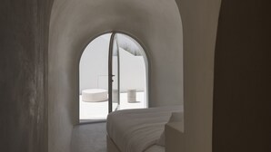 Un couloir étroit et voûté qui mène à une chambre à coucher, où se trouvent un lit et une fenêtre.
