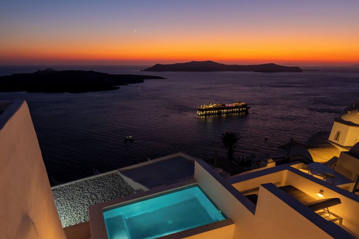 Une piscine sur le toit avec vue sur la mer et un bateau au coucher du soleil.