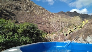 A swimming pool with a stone edge, surrounded by rocky terrain and sparse vegetation.