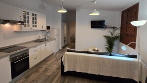 A modern kitchen with white cabinets, a dining area with a table and chairs, and a TV mounted on the wall.