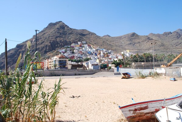 A coastal town with buildings on a hillside, a sandy beach, and boats.
