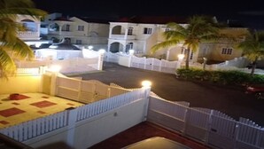 Un patio amurallado con una cerca blanca, palmeras y un edificio con varios arcos y balcones.