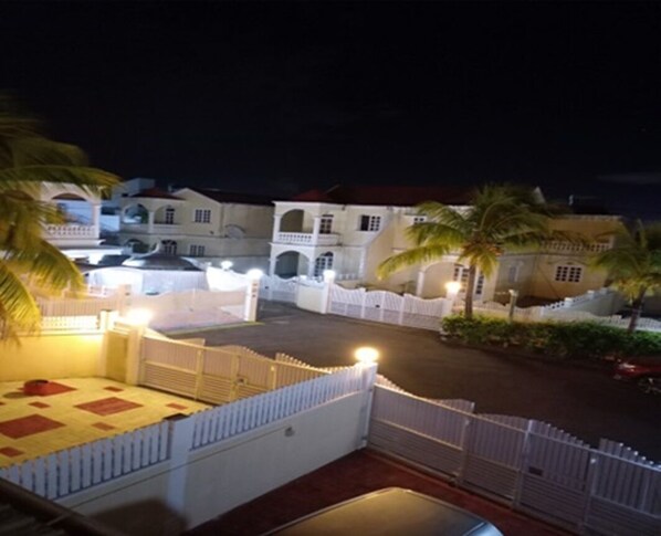 Un patio amurallado con una cerca blanca, palmeras y un edificio con varios arcos y balcones.
