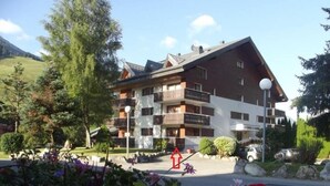 A multi-story hotel with balconies, surrounded by greenery and a mountainous backdrop.