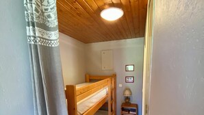 A small, cozy room with wooden bunk beds and a small table with a lamp.