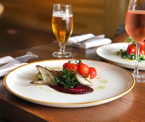 A dining table with plates of food, a glass of wine, and a fork and knife set.
