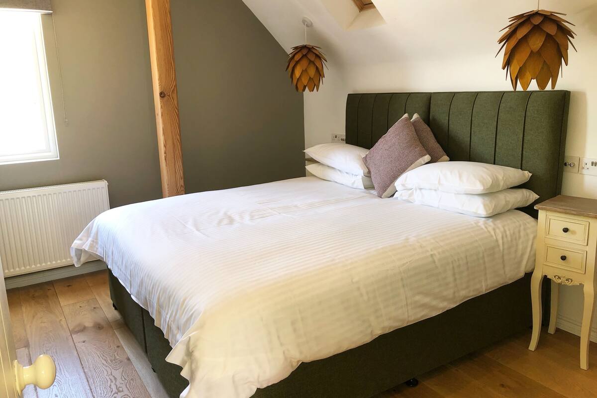 A bedroom with a large bed, a wooden headboard, two wall-mounted lamps, a bedside table, and a radiator.
