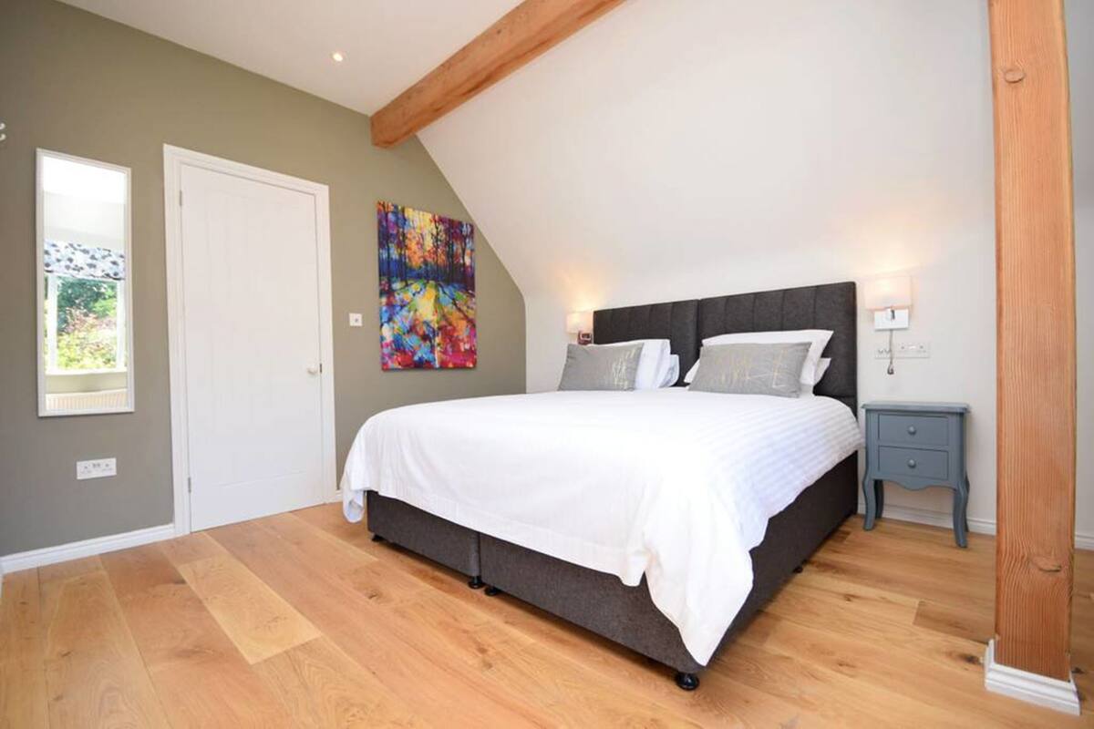 A bedroom with a large bed, a nightstand, a colorful painting, and a wooden ceiling beam.