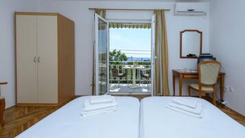 A hotel room with two beds, a wardrobe, a desk with a chair, a balcony with a view, and an air conditioning unit.