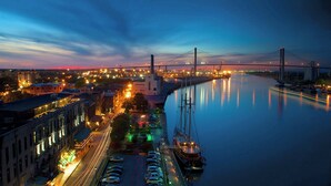 A nighttime cityscape with a bridge, calm river, and docked boats. - Aloft by Marriott Savannah Downtown Historic District (Savannah)